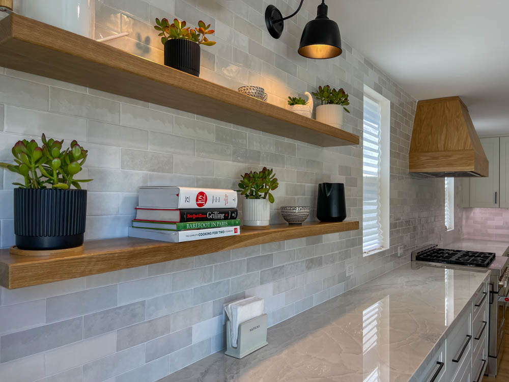 A newly remodeled kitchen with installed tile backsplash, upgraded countertop, and wall-mounted shelves and light fixture