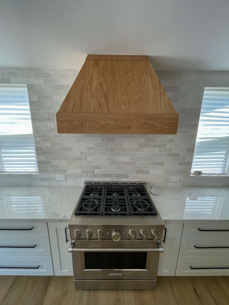 A newly remodeled kitchen with installed tile backsplash, upgraded countertop, stove oven, and an exhaust hood