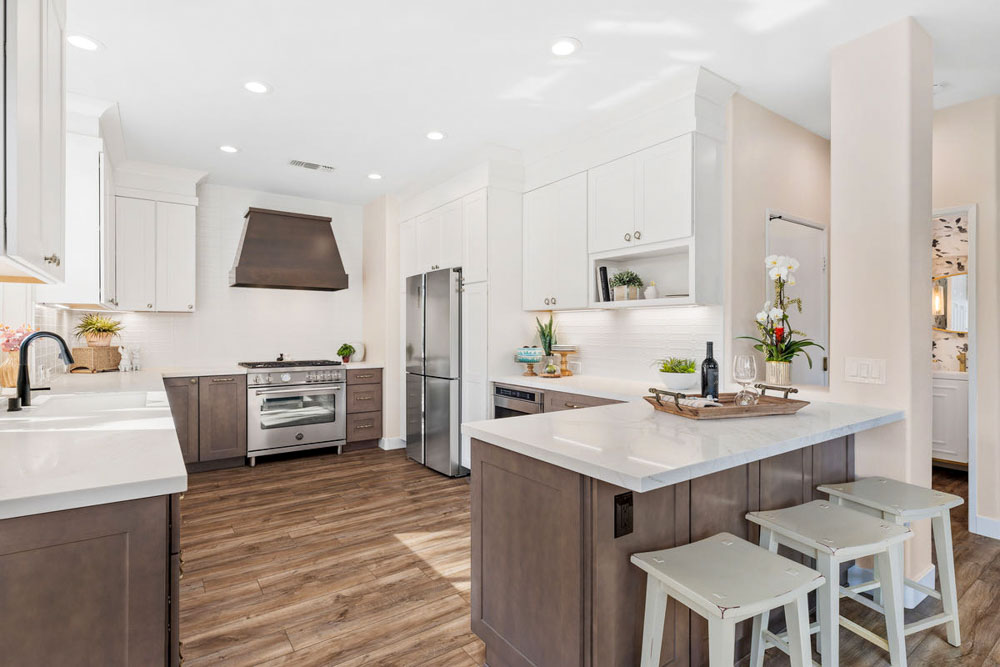 A remodeled kitchen with wood cabinets, exhaust hood, ceramic countertops, a bar island with stools.