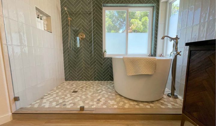 A remodeled bathroom with tiled shower backsplash, a wide shower room with glass partition, a freestanding bathtub and faucet