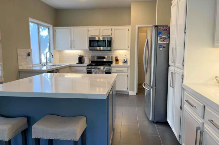 A remodeled U-shaped kitchen, porcelain countertops, tiled backsplash and refurbished white cabinets with recessed lighting