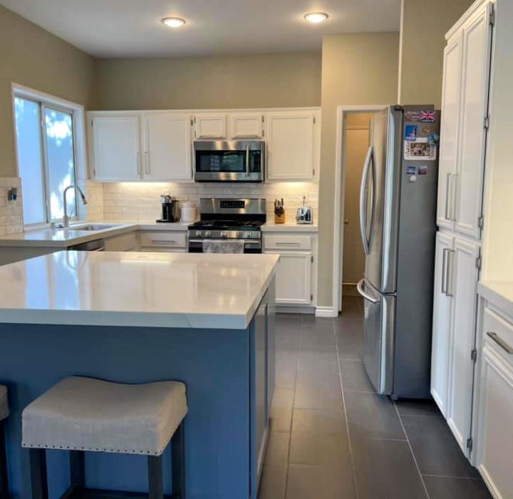 A remodeled U-shaped kitchen, porcelain countertops, tiled backsplash and refurbished white cabinets with recessed lighting