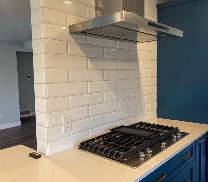 Upgraded built-in kitchen cooktop on a ceramic countertop, a tiled backsplash, blue drawers, and an exhaust hood